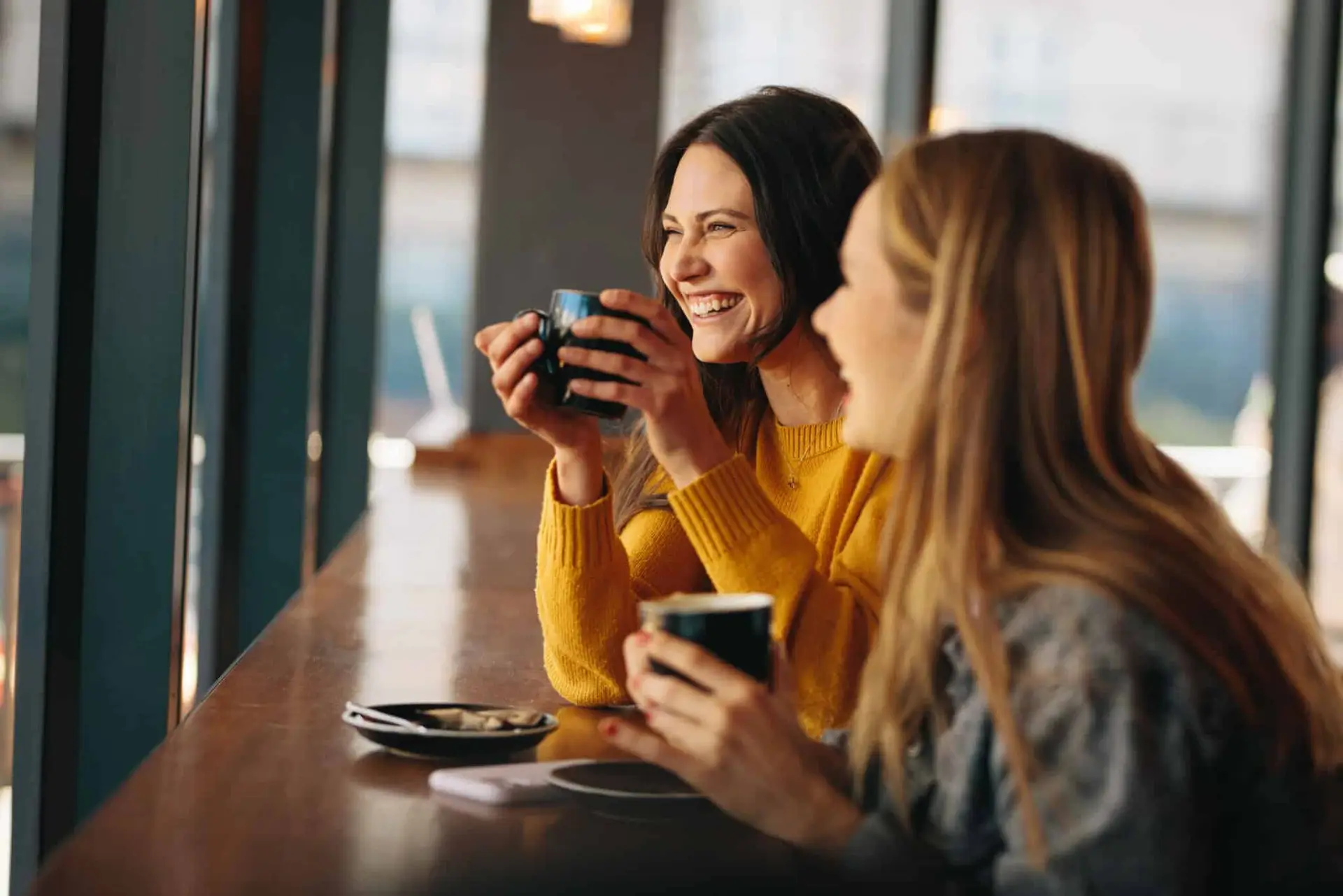 Two women enjoying coffee at a café, smiling and engaging in conversation, with a warm atmosphere and a focus on friendship and connection.