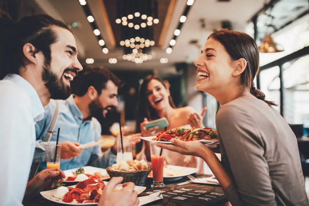 A group of friends laughing and enjoying a meal together at a restaurant, showcasing a lively and happy atmosphere.